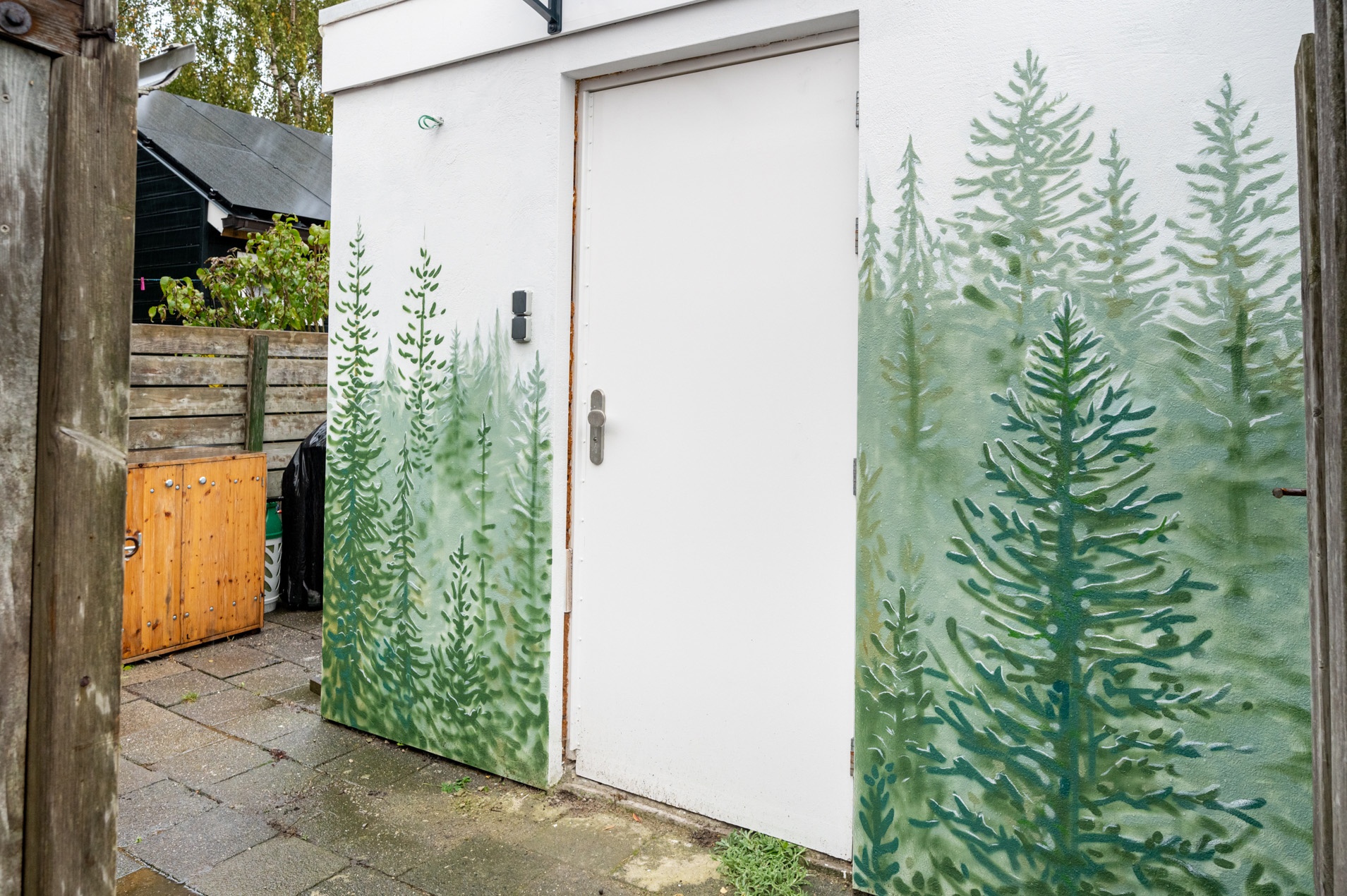 De ingang van de studio: een witte deur in een muur met geschilderde dennenbomen