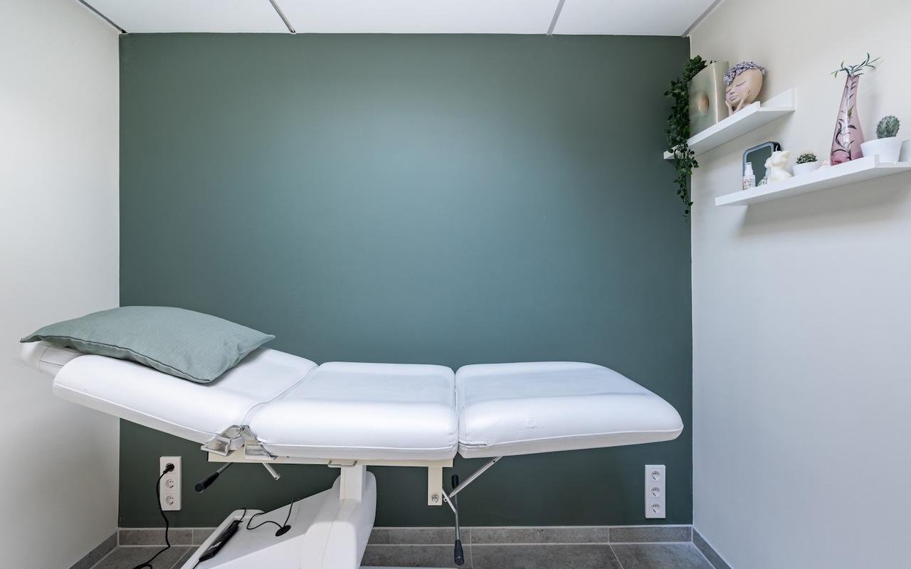 Witte behandeltafel met een saliegroen kussen tegen de groene wand